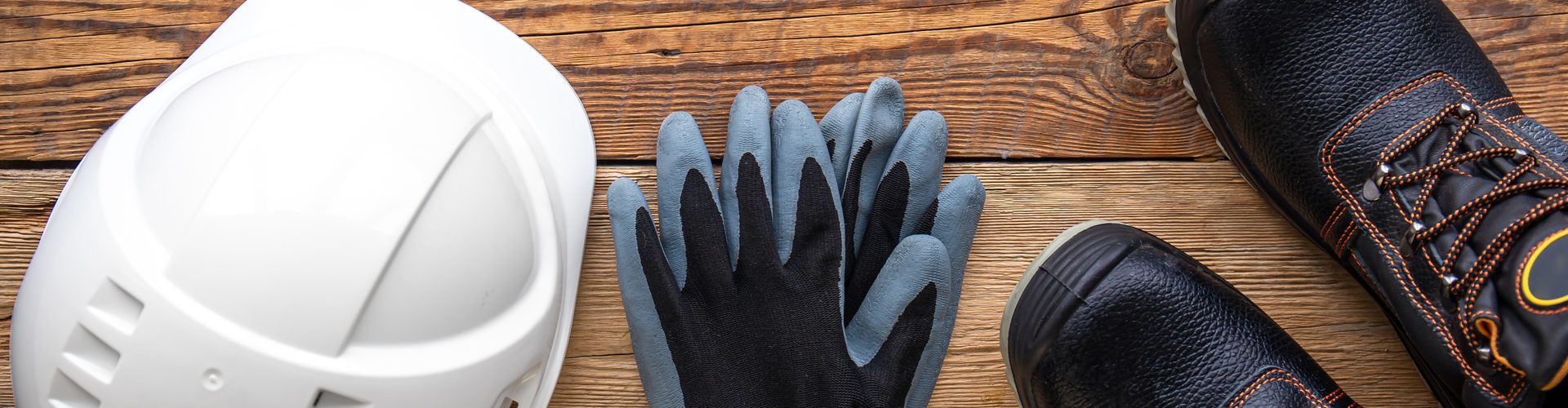 Work helmet, boots and gloves on a wooden background, top view, construction and special clothing concept.